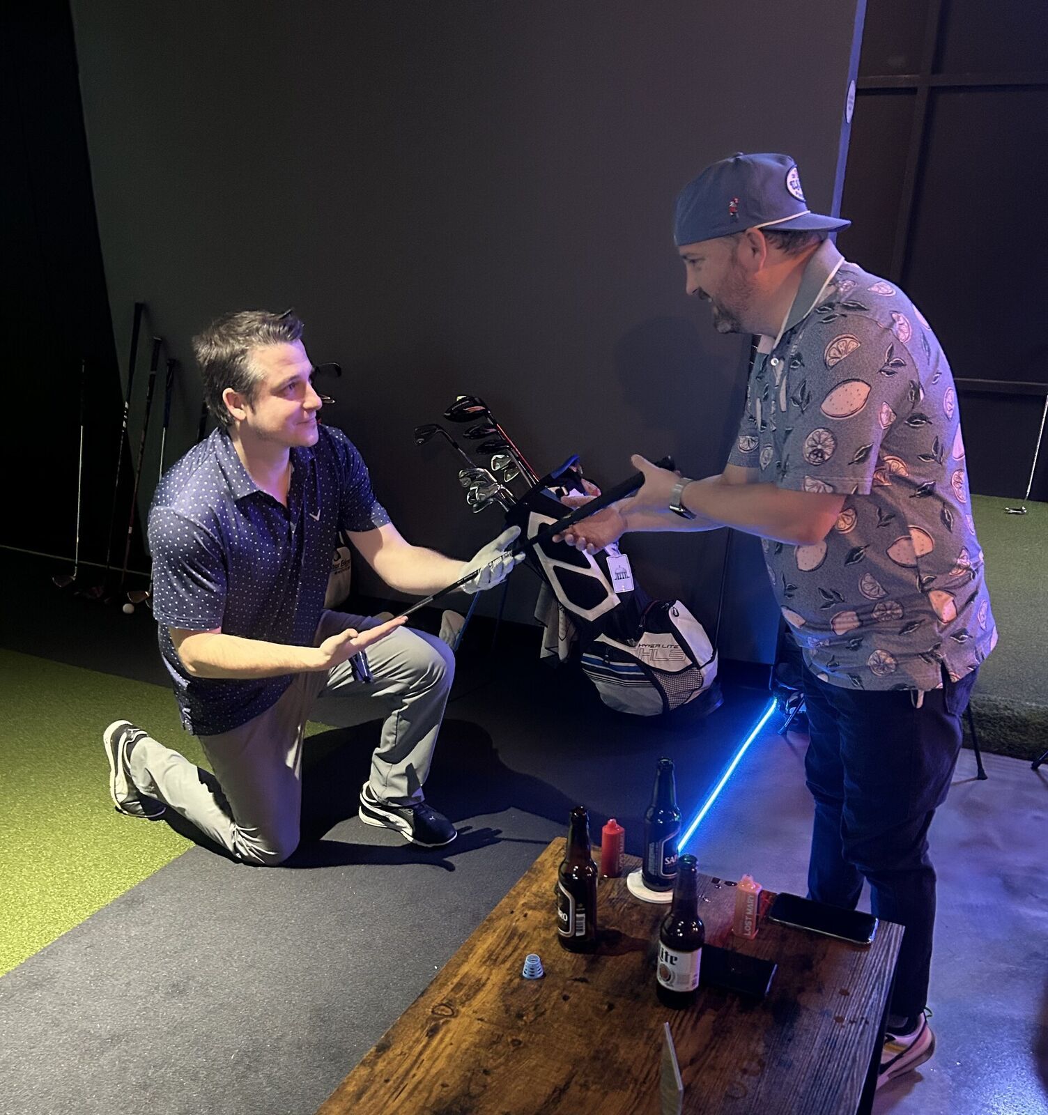 A player kneeling to hand a club from the rental bag to his buddy in the bay
