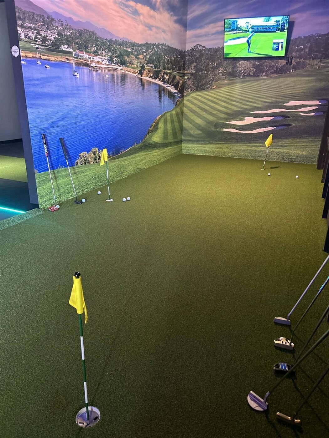 Indoor putting green with flags and a simulator screen in the background