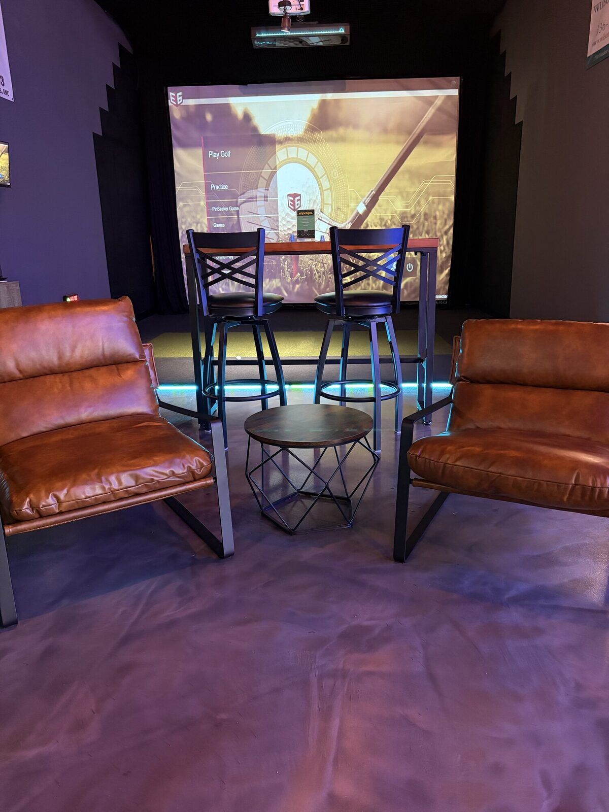 Leather lounge chairs and a table in front of a simulator bay at Grip It Virtual Golf